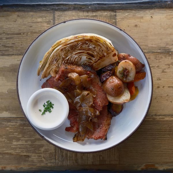 Corned beef with caramelized onions, roasted cabbage, potatoes, and a side of creamy sauce.