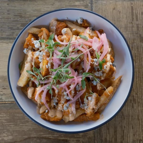 A bowl of buffalo chicken fries with blue cheese, pickled onions, and microgreens from The Corner Drafthouse.
