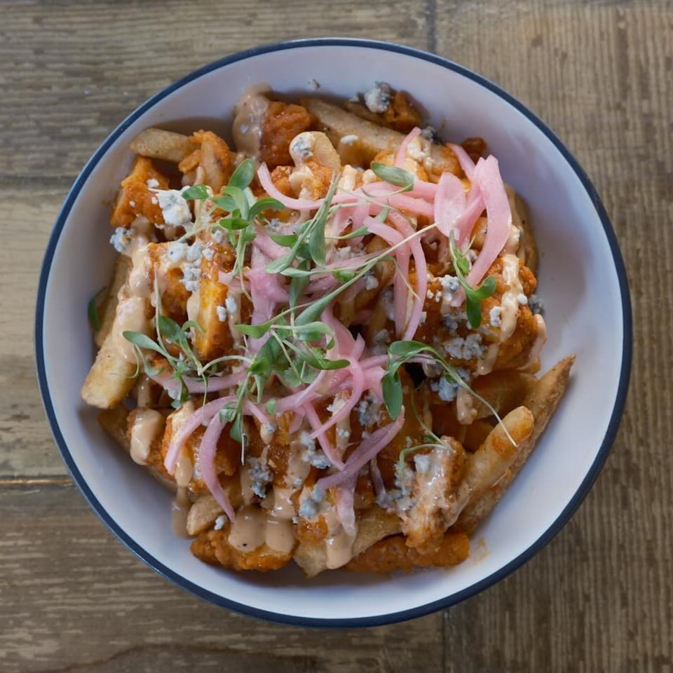 A bowl of buffalo chicken fries with blue cheese, pickled onions, and microgreens from The Corner Drafthouse.