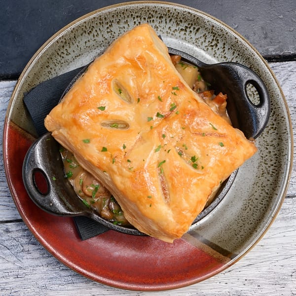 Golden-brown pot pie with a flaky crust, served in a cast iron dish on a rustic plate.