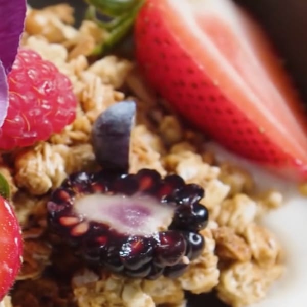 Close-up of granola with fresh raspberries, blueberries, sliced strawberries, and a blackberry.