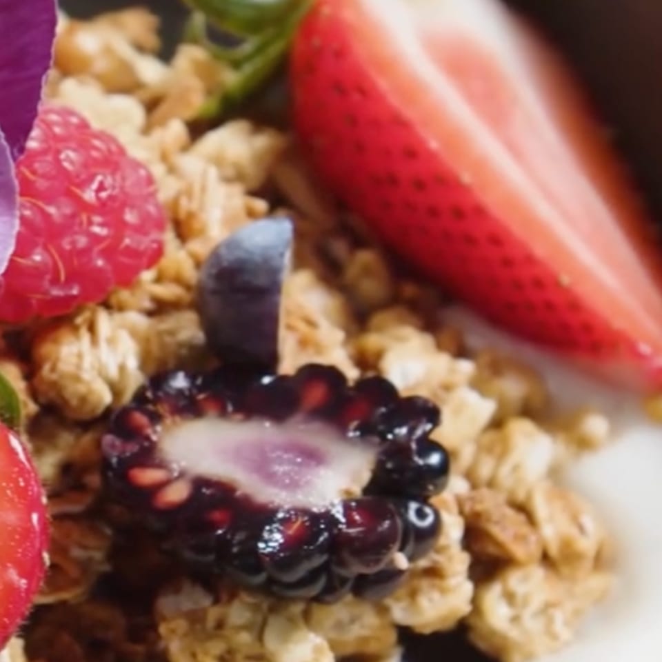 Close-up of granola with fresh raspberries, blueberries, sliced strawberries, and a blackberry.