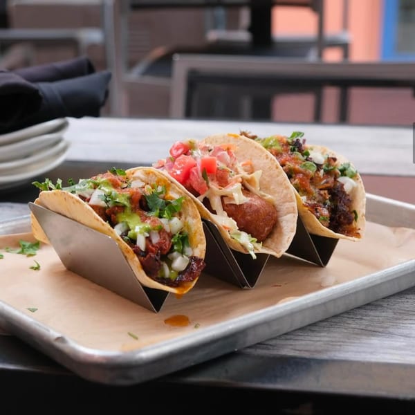 Three gourmet tacos with various fillings and toppings, served on a metal tray at The Corner Drafthouse.