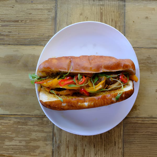 A toasted sub sandwich filled with colorful bell peppers, onions, and microgreens on a white plate.