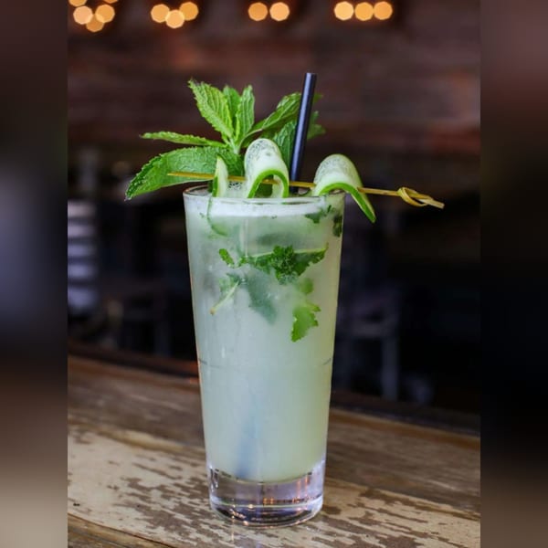 A refreshing mojito with mint and cucumber garnish sits on a rustic wooden bar.