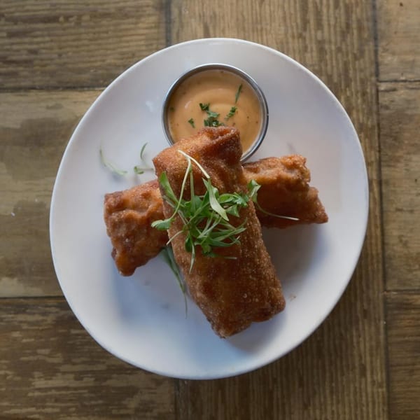 Two crispy fried spring rolls with microgreens, served with a side of creamy dipping sauce.