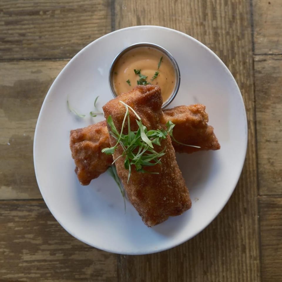 Two crispy fried spring rolls with microgreens, served with a side of creamy dipping sauce.