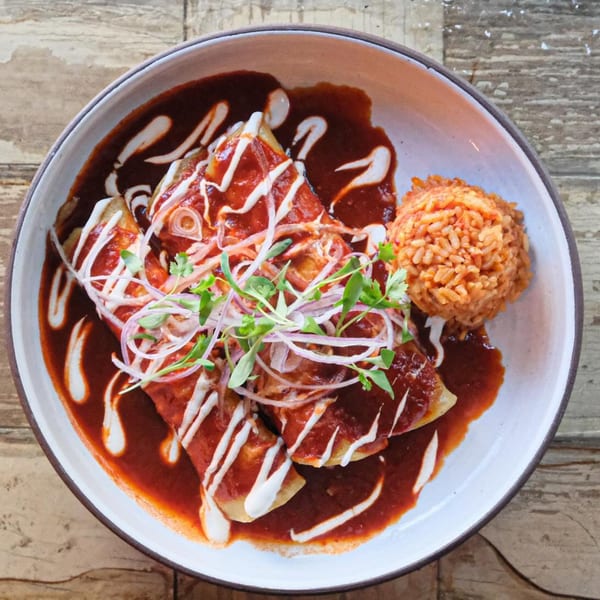 Enchiladas with red sauce, sour cream, red onions, and microgreens, served with a side of rice.