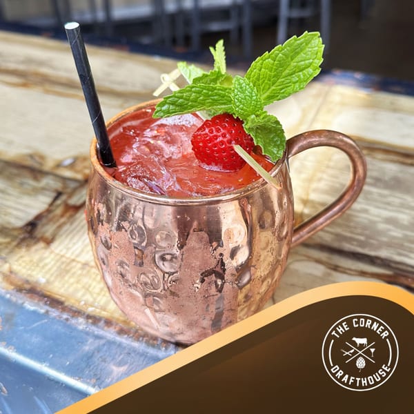A strawberry cocktail in a copper mug, garnished with mint and a strawberry, on a wooden table.
