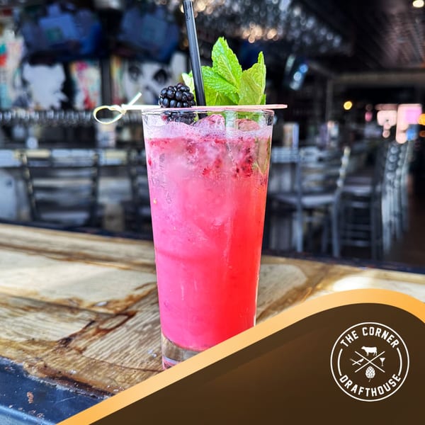 Pink cocktail with blackberries and mint on a wooden bar at The Corner Drafthouse.
