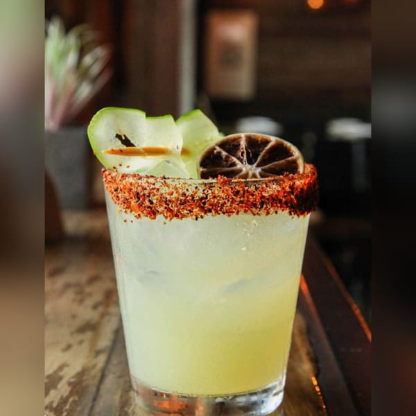 A margarita with a chili-salt rim, garnished with cucumber slices and a dried lime wheel.